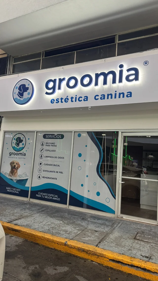 Fachada real de Groomia: rótulo iluminado, isotipo y viniles azules